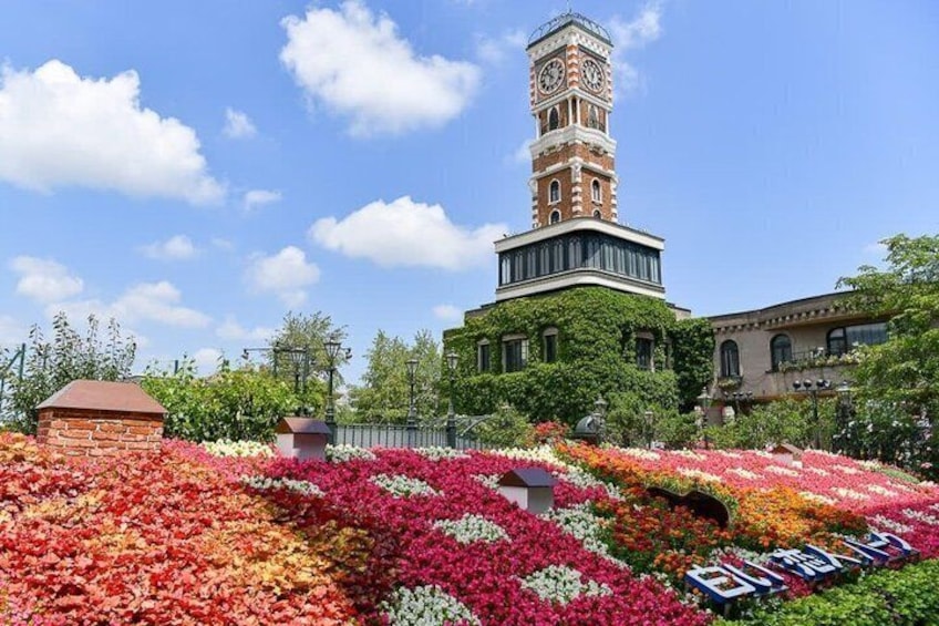 A tower with a clock, surrounded by colorful flower beds and greenery. 1