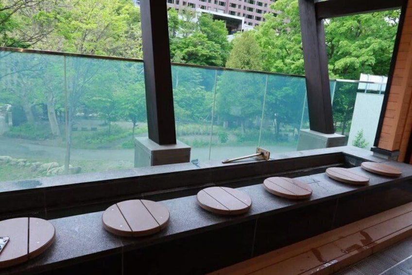 A wooden bench with a glass railing, a view of trees, and a building in the background. 5