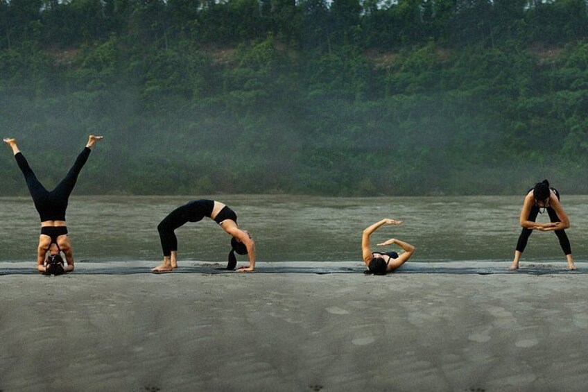 Four people performing yoga poses on a concrete surface near a body of water with trees in the background. 3