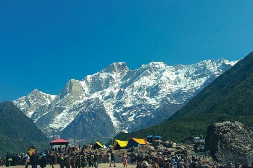 A mountainous landscape with snow-capped peaks, tents, and a crowd of people. 3