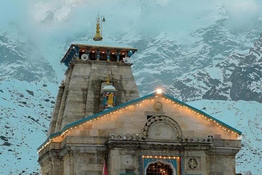 A stone building with a pointed roof, surrounded by snow-covered mountains. 1