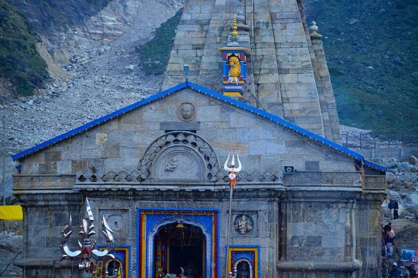 A stone temple with a blue roof, a central deity statue, and a trident symbol. 2