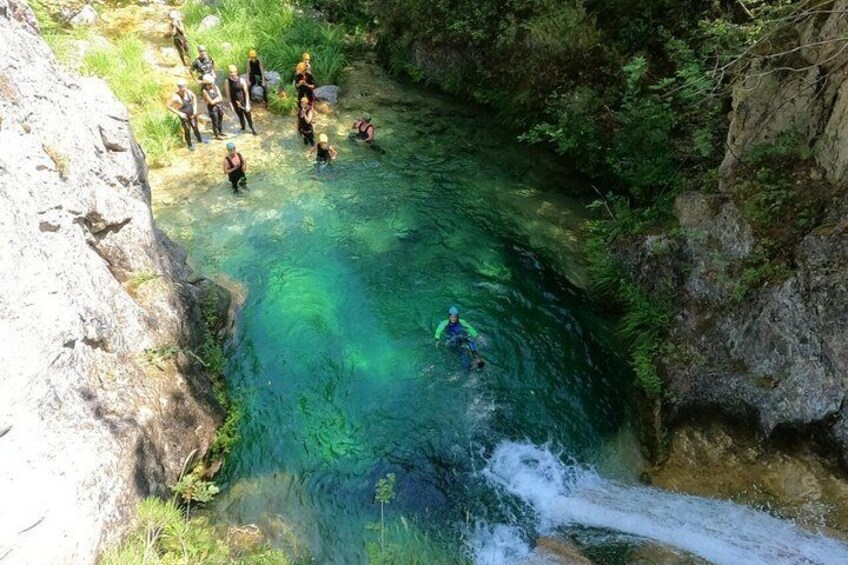 A group of people kayaking in a clear river surrounded by rocky cliffs and greenery. 5