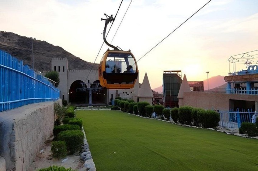 A cable car moving along a cable, a blue fence, and a green lawn. 1