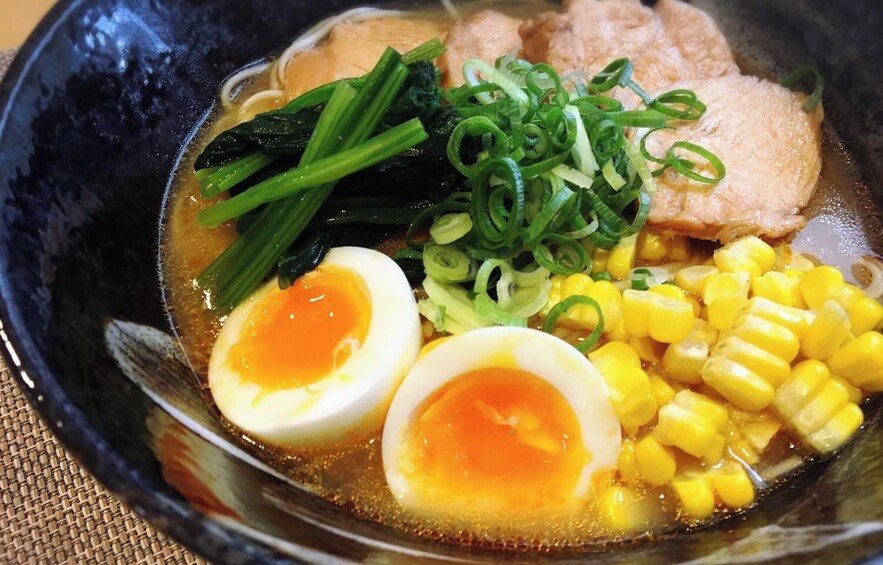 A bowl of ramen with sliced boiled eggs, corn, green onions, and seaweed. 5