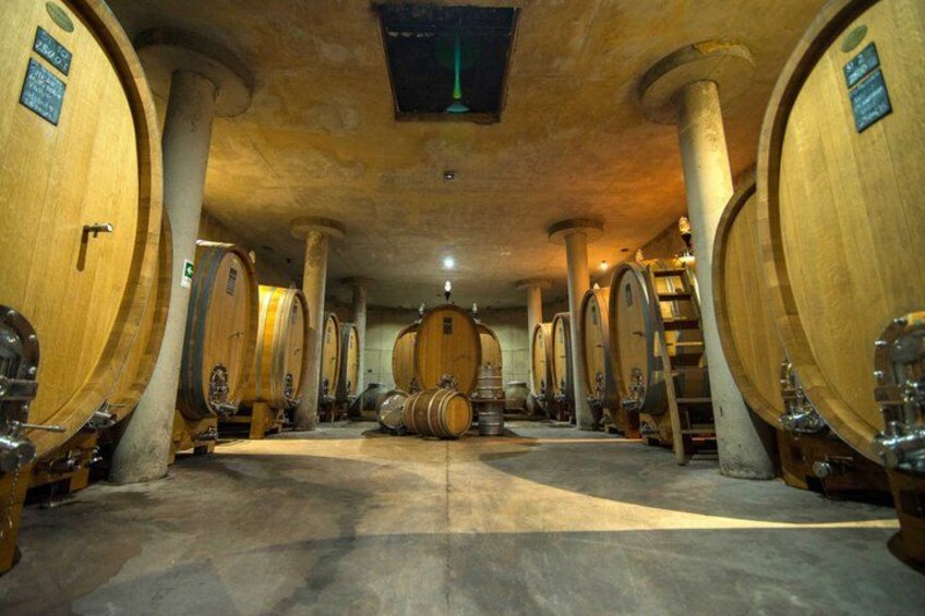 A cellar with wooden wine barrels, stone pillars, and a central staircase. 3