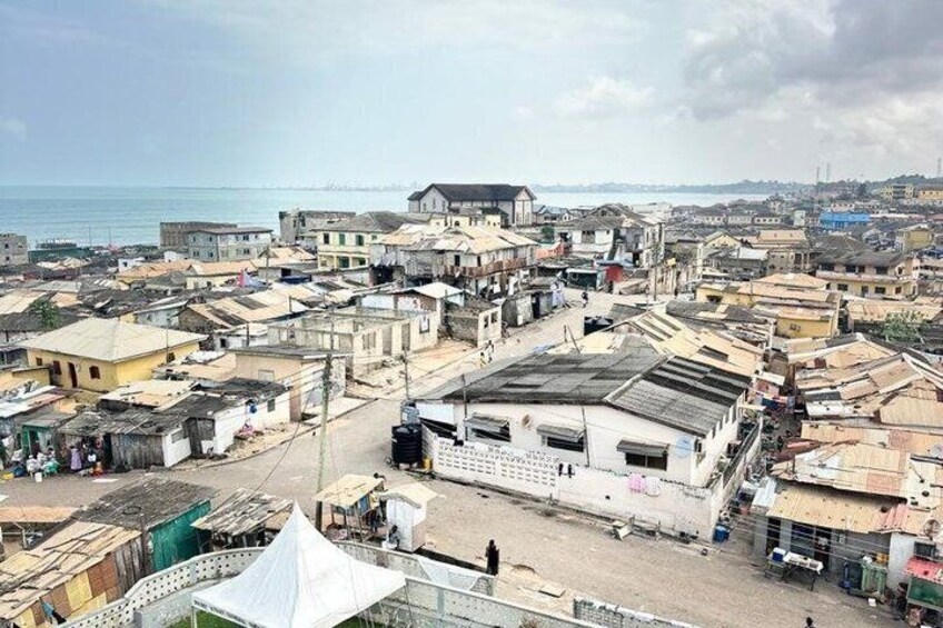 A coastal urban area with densely packed buildings, a large white building in the center, and a body of water in the background. 3