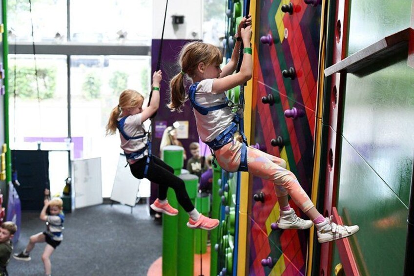 Children climbing a colorful wall in an indoor climbing area. 2