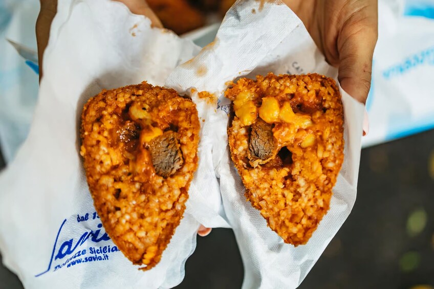 A person holding a half-eaten food item with a crispy, golden-brown crust and a visible filling of meat and vegetables. 3
