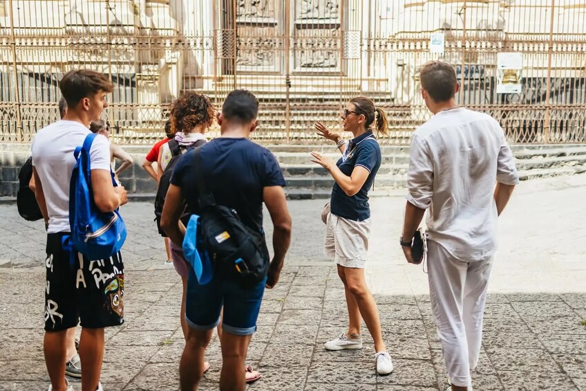 A group of people standing on a stone-paved area in front of ornate metal gates. 1