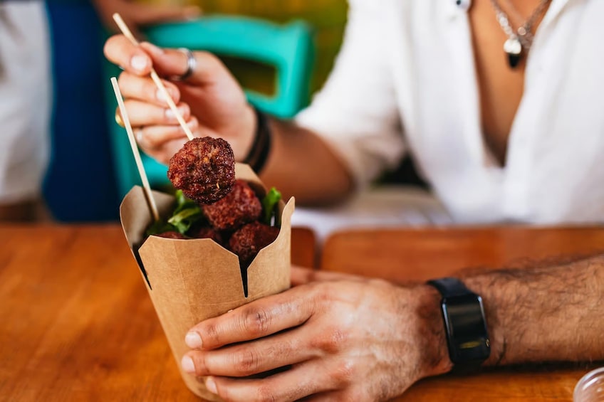 A person holding a paper cup with skewers of food. 5