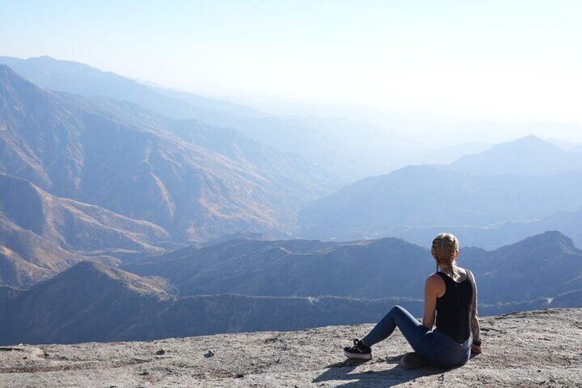 A person sitting on a mountain ridge overlooking a valley with distant mountains. 4