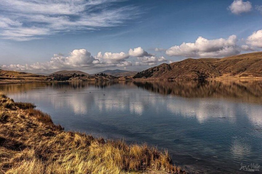 A calm lake with grassy banks, distant hills, and a partly cloudy sky. 4