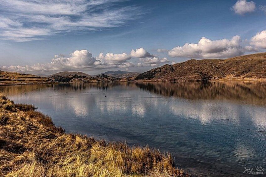 A calm lake with grassy banks and distant hills under a partly cloudy sky. 5