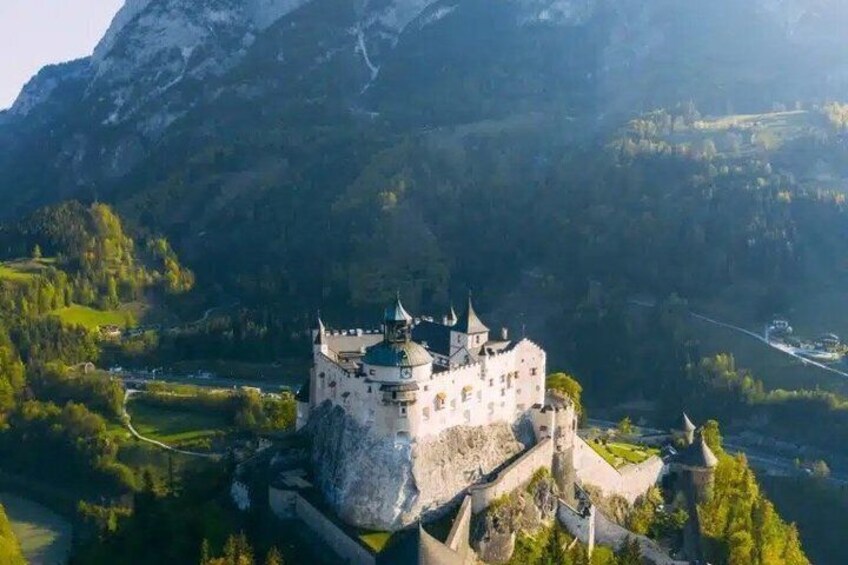 A castle on a hill with a river in the foreground and mountains in the background. 4