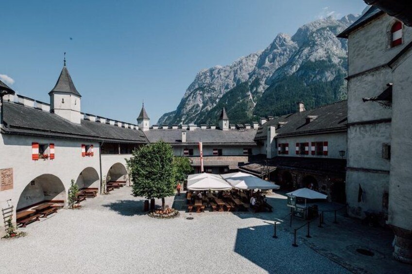 A courtyard with buildings, a tree, and mountains in the background. 3