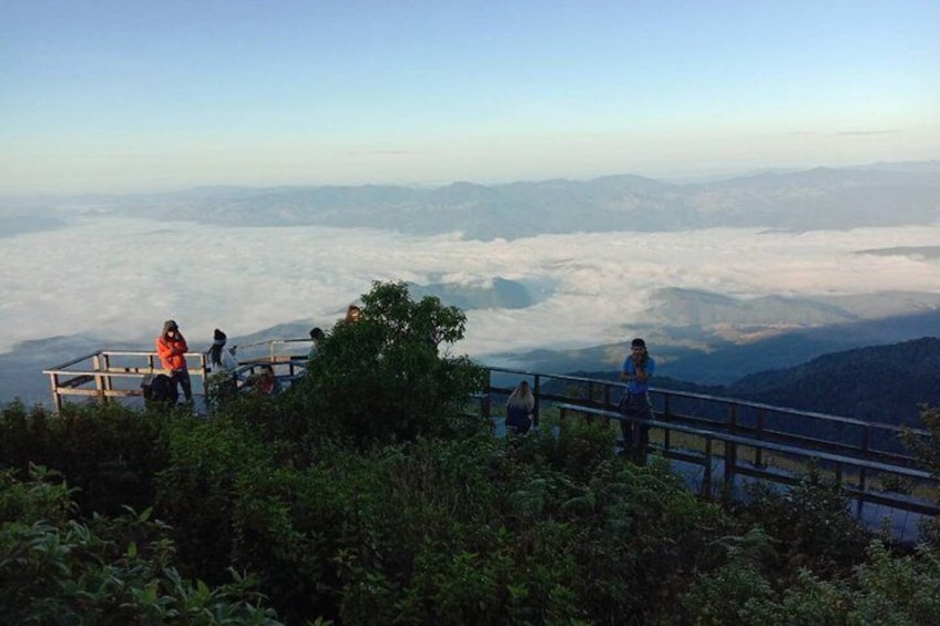 A group of people on a wooden observation deck overlooking a valley with a cloud-covered landscape. 5
