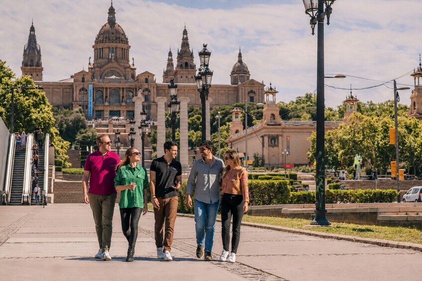 A group of people walking on a sidewalk with a large historical building in the background. 4