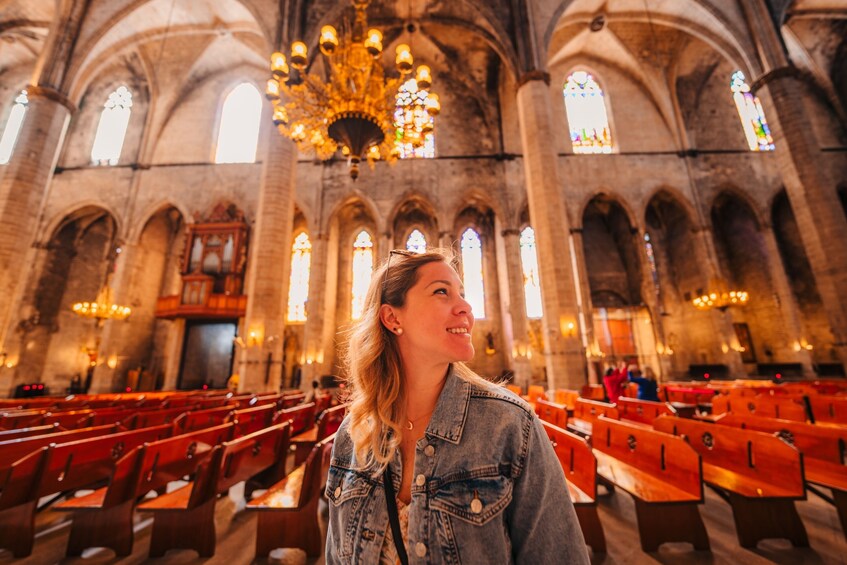 A woman in a denim jacket inside a church with red pews and stained glass windows. 5