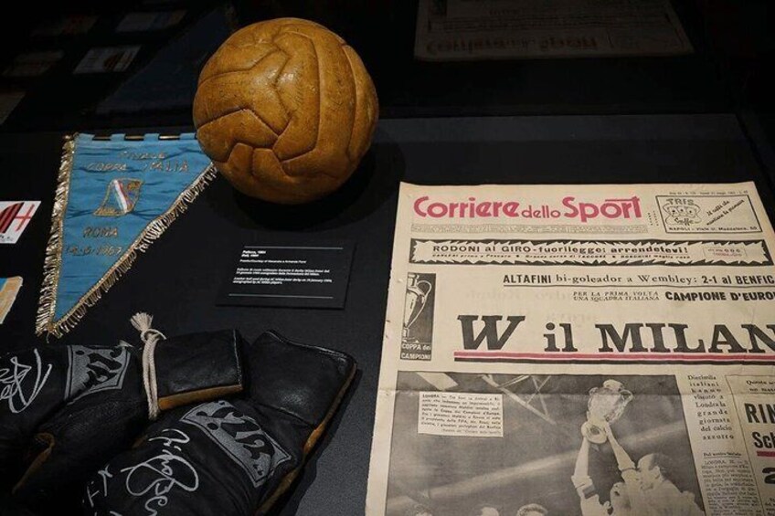 A soccer ball, a pair of black and white sneakers, a blue and gold ribbon, and a newspaper with Italian text. 4