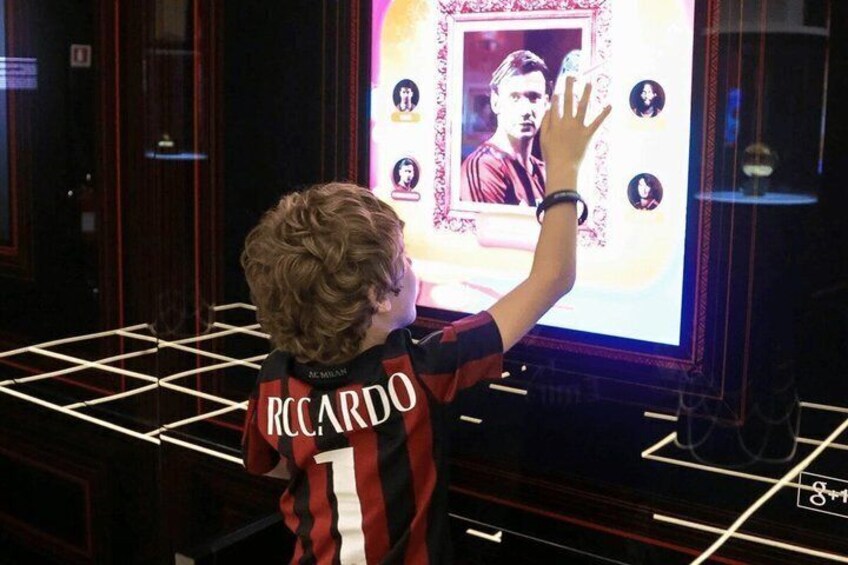 A child wearing a sports jersey with the name 'RCCARDO' and number '1' standing in front of a display with a framed picture and some icons. 2