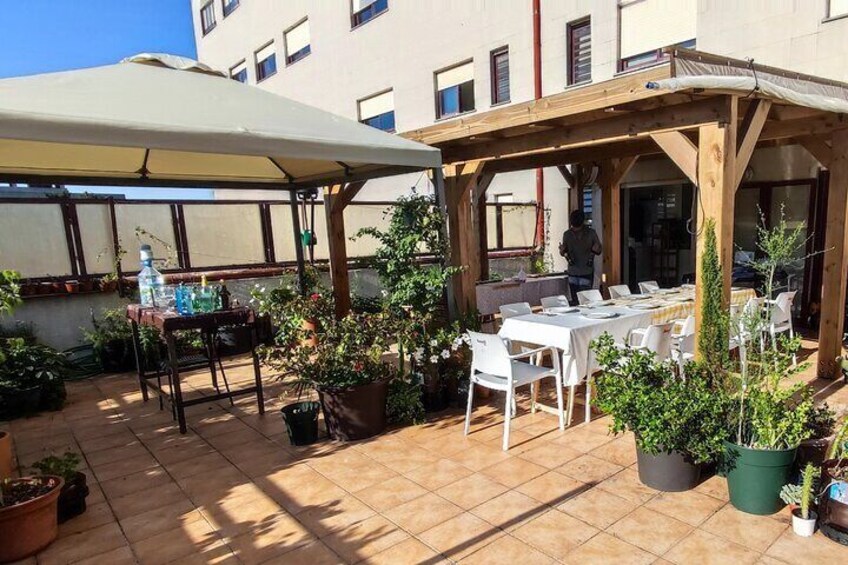 An outdoor patio with tables and chairs, surrounded by potted plants and a wooden pergola. 3