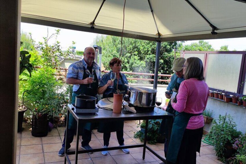 A group of people around a table with cooking equipment, under a tent in a garden. 5