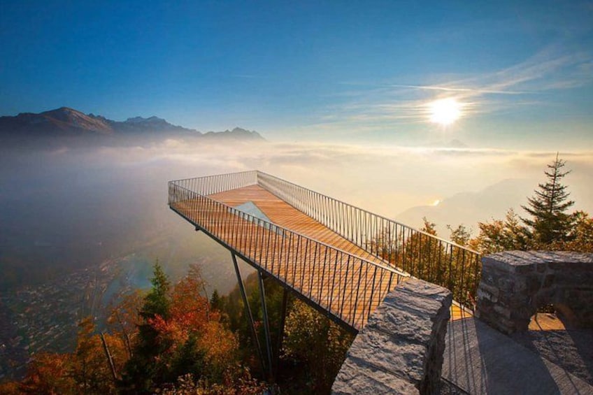 A wooden observation deck with a metal railing overlooking a valley and mountains. 2