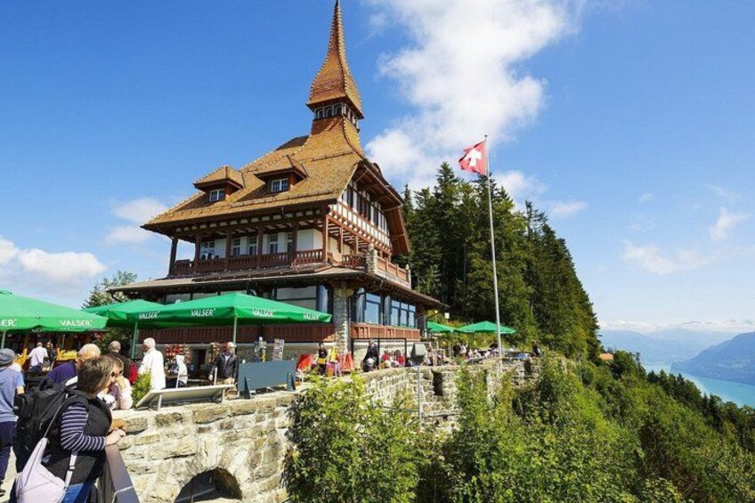 A traditional wooden chalet with a steep roof, surrounded by lush greenery and a clear sky. 2