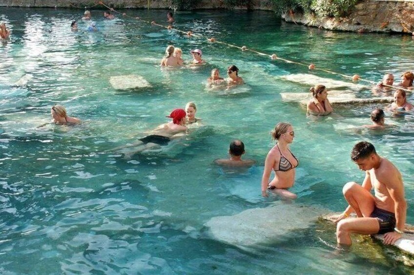 A group of people in a swimming pool with clear water, some standing and others sitting on rocks. 4