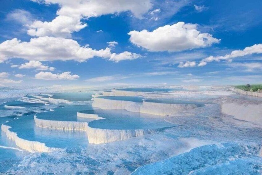 Terraced mineral pools, clear skies, and distant greenery. 2