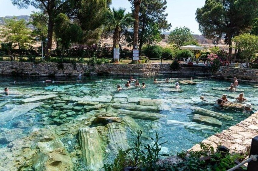 A clear pool with people swimming, surrounded by trees and a stone wall. 5