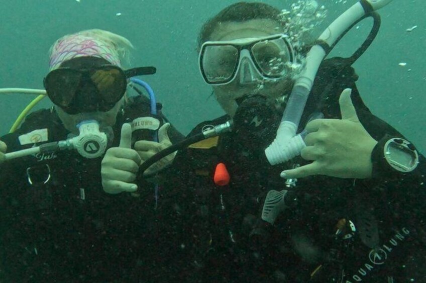 Two scuba divers underwater, one pointing at the other, with scuba gear and a regulator. 2