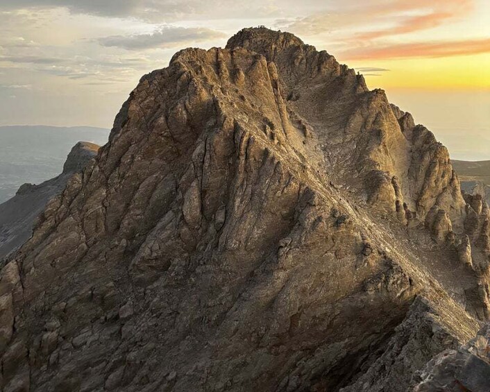 A rugged mountain peak with steep, rocky slopes and a clear sky in the background. 1