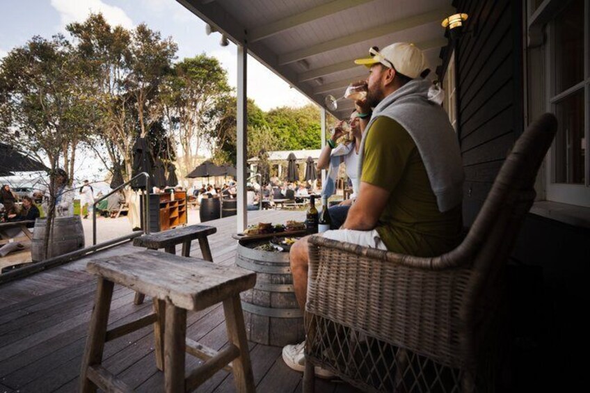 A wooden deck with a wicker chair, a wooden table, and a person sitting. 1