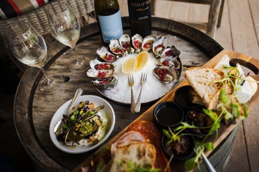 A wooden table with a variety of dishes, including oysters, a salad, and bread, accompanied by wine glasses and a bottle of wine. 4