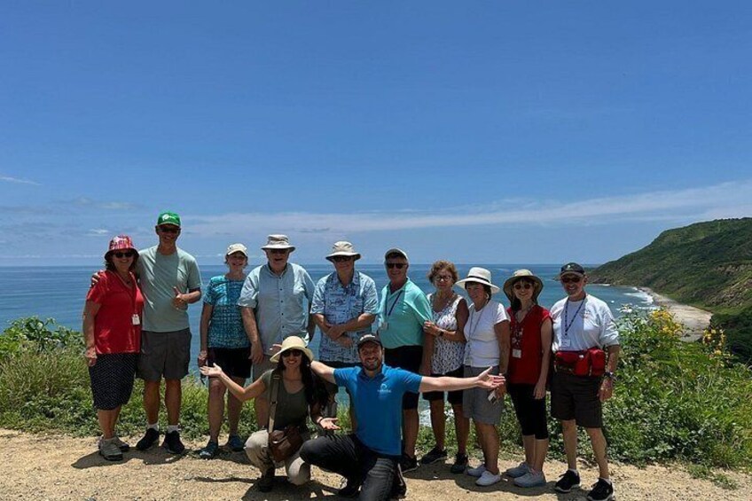 A group of people standing on a coastal path with a view of the ocean and hills in the background. 2
