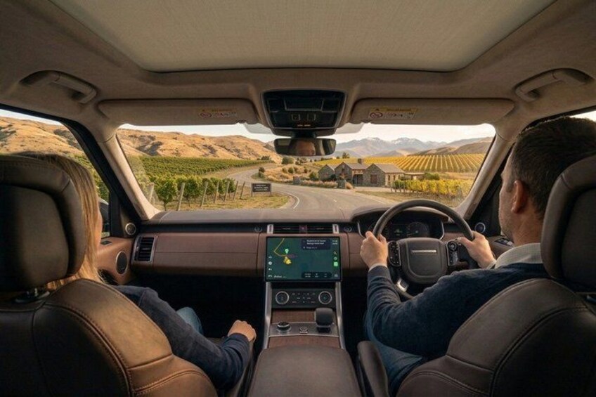 A car interior with a digital dashboard, leather seats, and a view of a vineyard through the windshield. 3