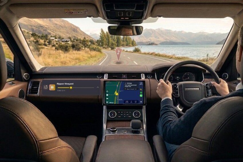 A car interior with a digital dashboard, leather seats, and a view of a road with mountains and a lake. 1