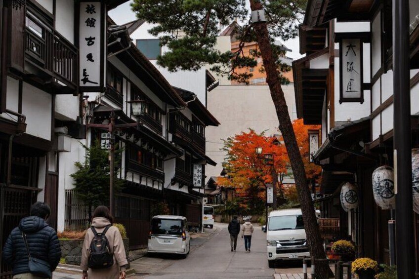 A traditional Japanese street with pedestrians, a white van, and autumn foliage. 3