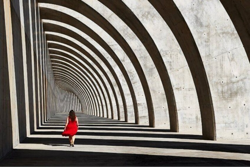 A person in a red dress walking through a tunnel with concentric arches. 2