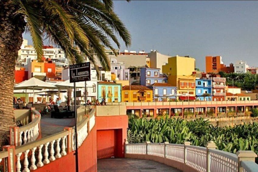 A colorful coastal town with a palm tree, a sign reading 'La Azqueta,' and a waterfront promenade. 1
