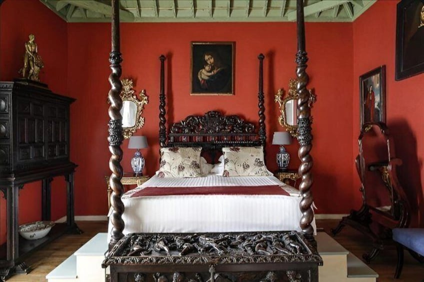 A four-poster bed with ornate carvings, a red wall, and a painting above it. 5