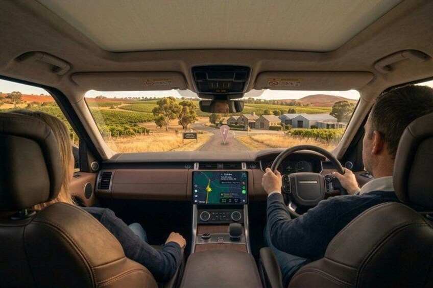A car interior with a digital dashboard, leather seats, and a view of a rural landscape with fields and houses. 1