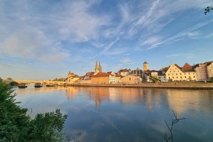 A calm river reflecting buildings, a prominent church spire, and a bridge. 5