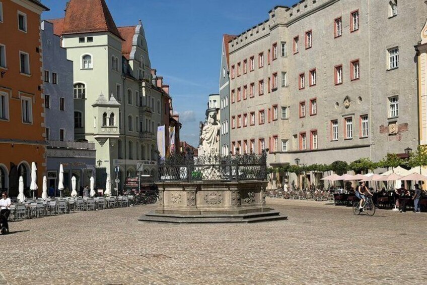A cobblestone square with a central fountain, surrounded by historic buildings with red window frames. 2