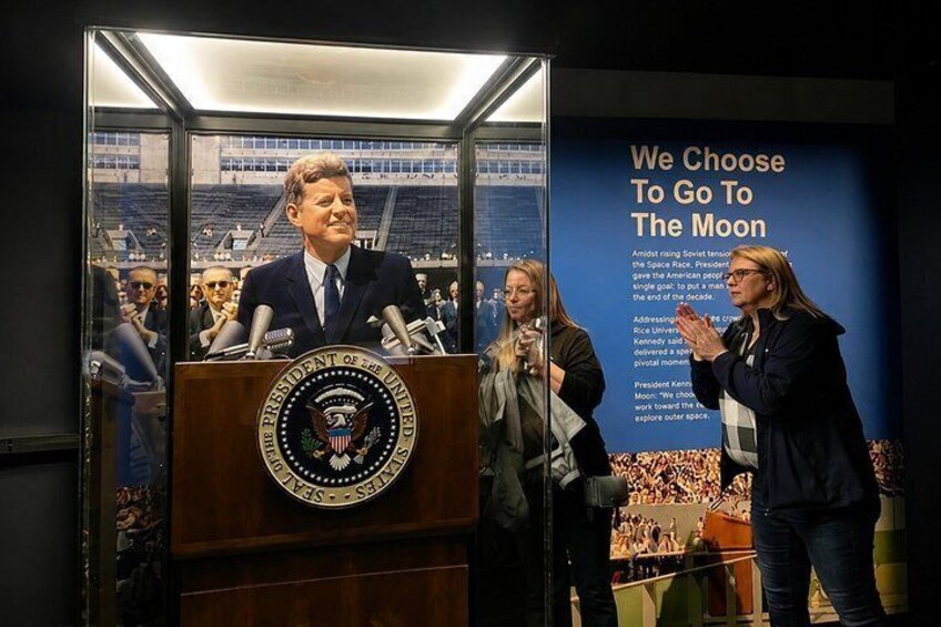 A person standing at a podium with a seal, and a poster in the background. 5