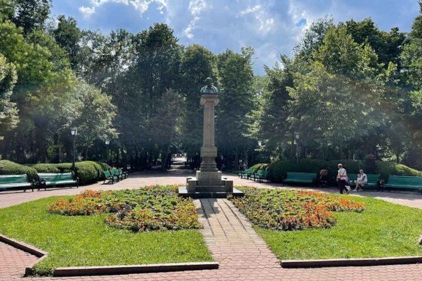 A park with a central monument, green lawns, flower beds, and benches. 3