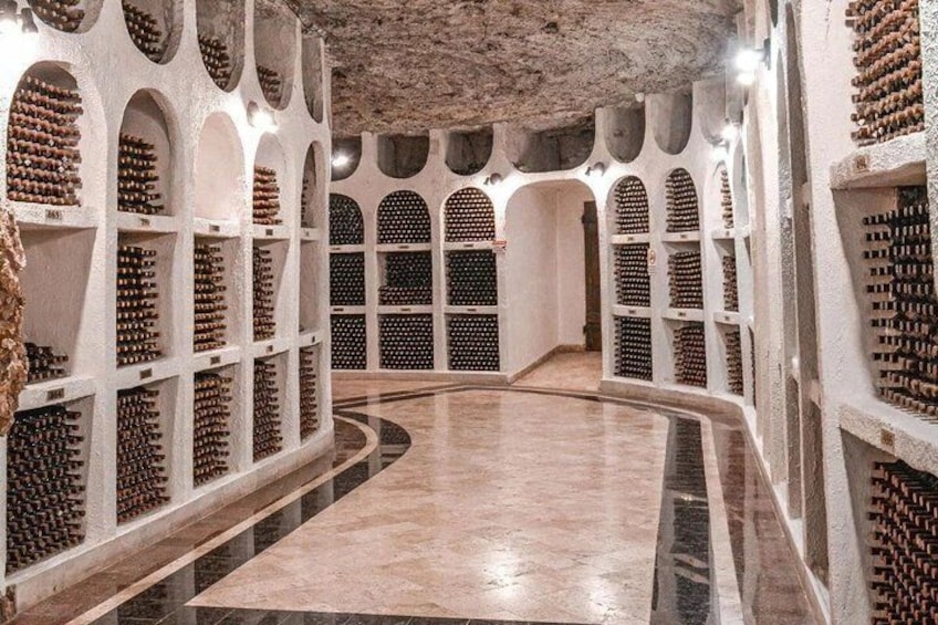 A wine cellar with rows of wine bottles, arched ceilings, and a polished floor. 1