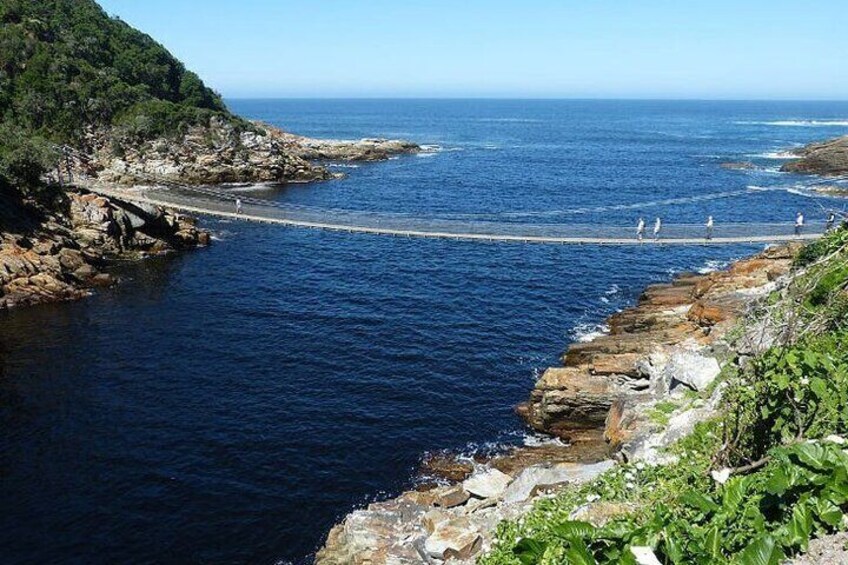 A coastal landscape with rocky cliffs, a pier extending into the sea, and a clear sky. 5